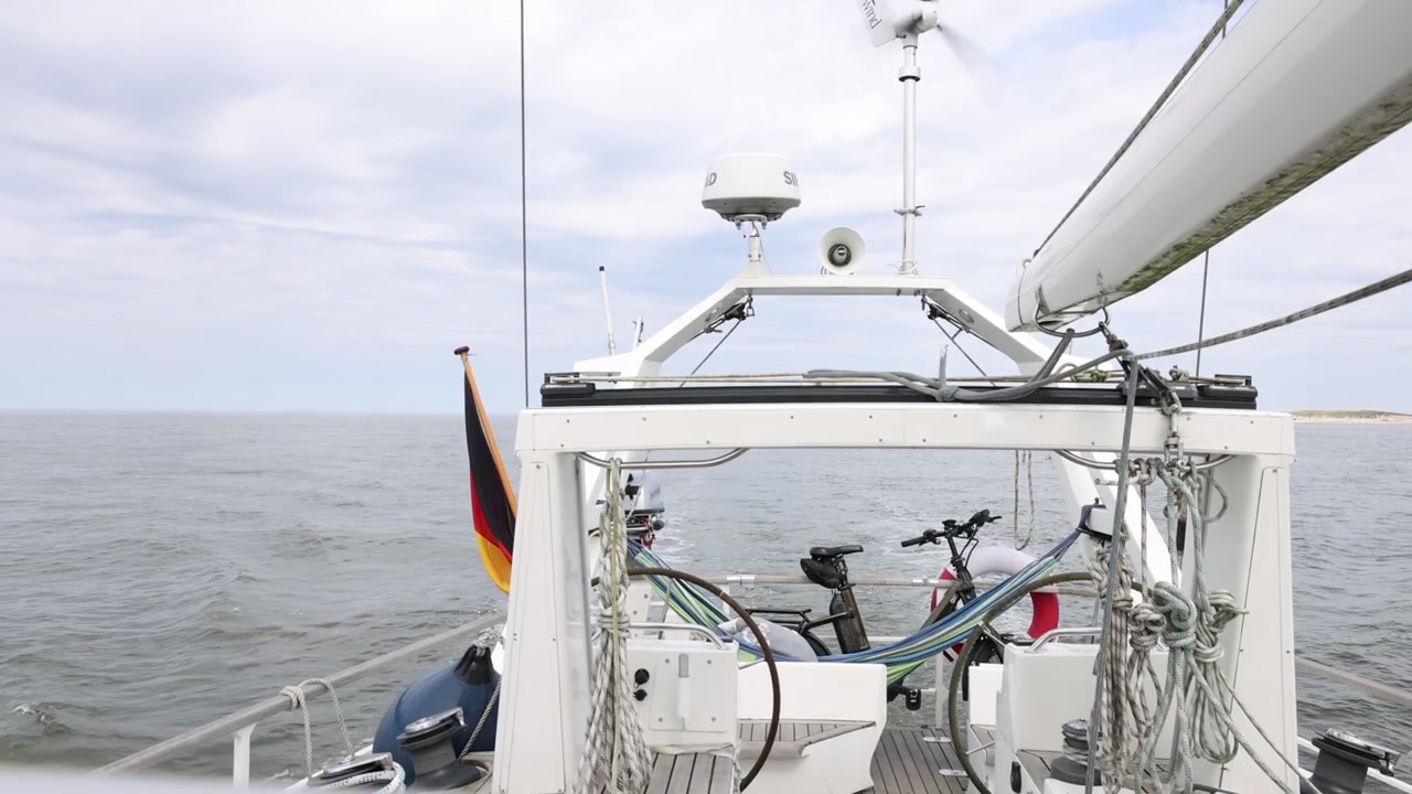 Vista stabile da barca a vela che mostra il movimento dell'albero, il mare e una turbina eolica offshore.