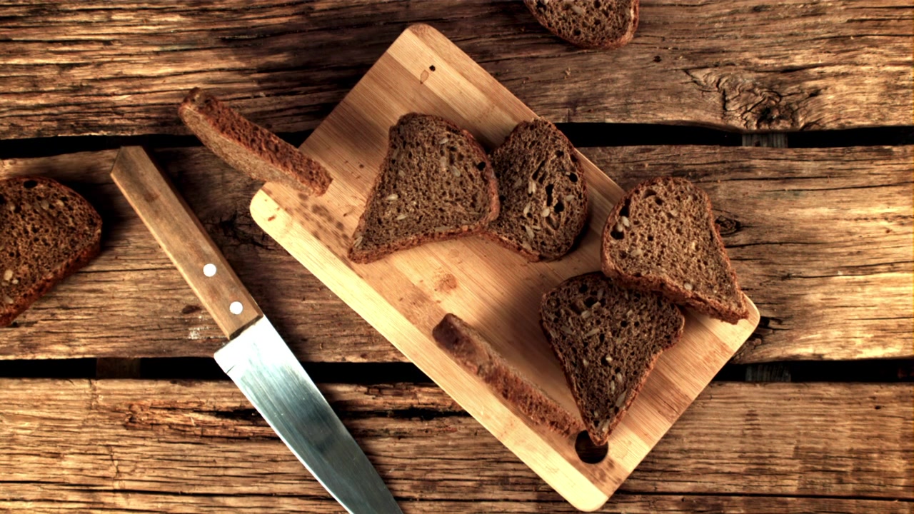 Slices of Dark Rye Bread Falling onto a Wooden Cutting Board