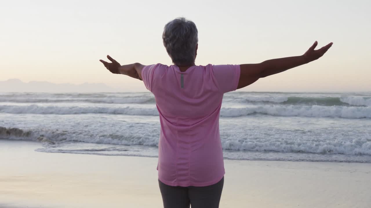 vista trasera de una mujer mayor afroamericana con los brazos abiertos de pie en la playa