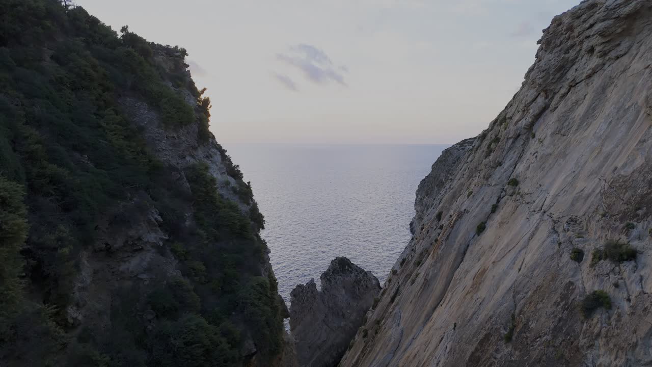 A drone descends through Xaqqa Valley with sun rays hitting the lens, revealing the rocky valley floor framed by steep cliffs and warm sunset light