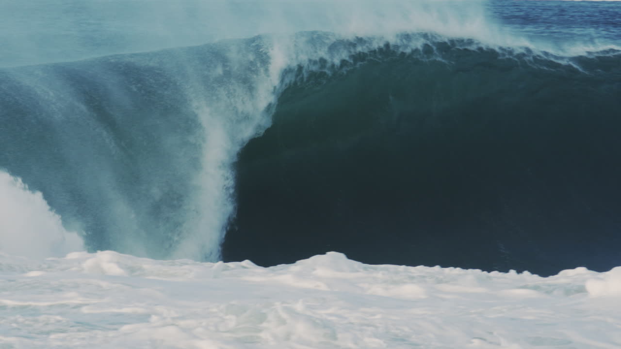 Thick ocean wave rolls and erupts with exploding spray and suspended droplets, slow motion telephoto