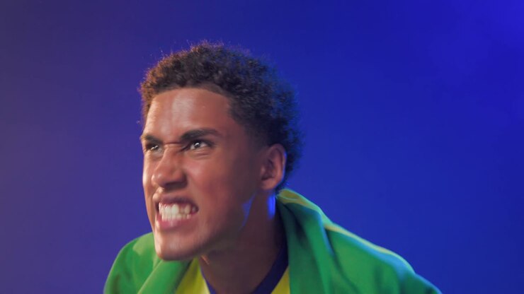 African American man lifting Brazilian flag initiating cheer wearing yellow jersey in studio