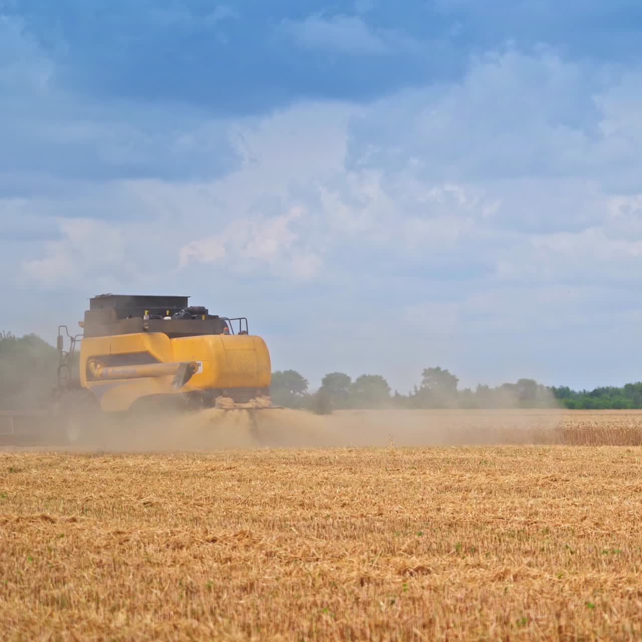 Yellow harvester hardly seen in the dusty clouds of straw flying off the machine. Working techniques in the beautiful nature scenery