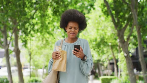 african american businesswoman eating and using smartphone