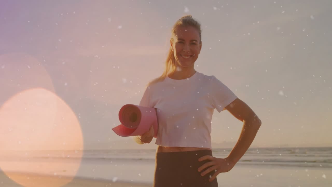 Sonnenaufgangslicht erzeugt Lens Flares, während ein Fitnesstrainer mit einer pinken Yogamatte am Strand für eine Anzeige entlanggeht.