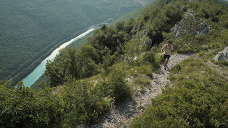 excursionista con una mochila caminando por un camino rocoso en sabotín de montaña, vista superior, gran vista de un valle con un río torquoise y bosques verdes