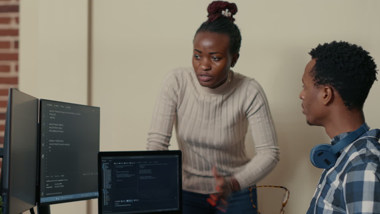 Database developer removing glasses while explaining algorithm to colleague coder pointing at running code