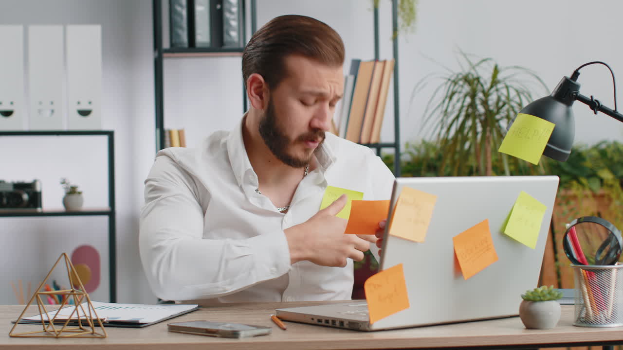 Tired sad exhausted businessman working on laptop at office with many sticker tasks panic attack