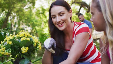 Smiling-caucasian-mother-and-daughter-gardening,-talking-and-holding-yellow-flowers