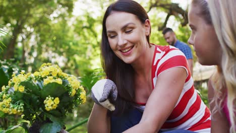 madre y hija caucásicas sonrientes jardinería, hablando y sosteniendo flores amarillas