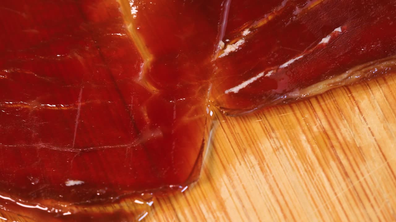 macro shot de jamón serrano español aceitoso de alta calidad girando sobre tablero de madera, vista de cerca desde arriba