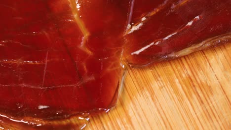 macro shot of oily high quality spanish serrano ham rotating on wooden board, close up view from above