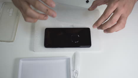 man carefully applies the screen protector on a smartphone after applying the glue