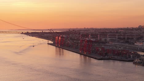 Vista-Aérea-Panorámica-De-Las-Grúas-Portuarias-En-El-Río-Tajo-En-Lisboa,-Portugal,-Estableciéndose-Al-Atardecer