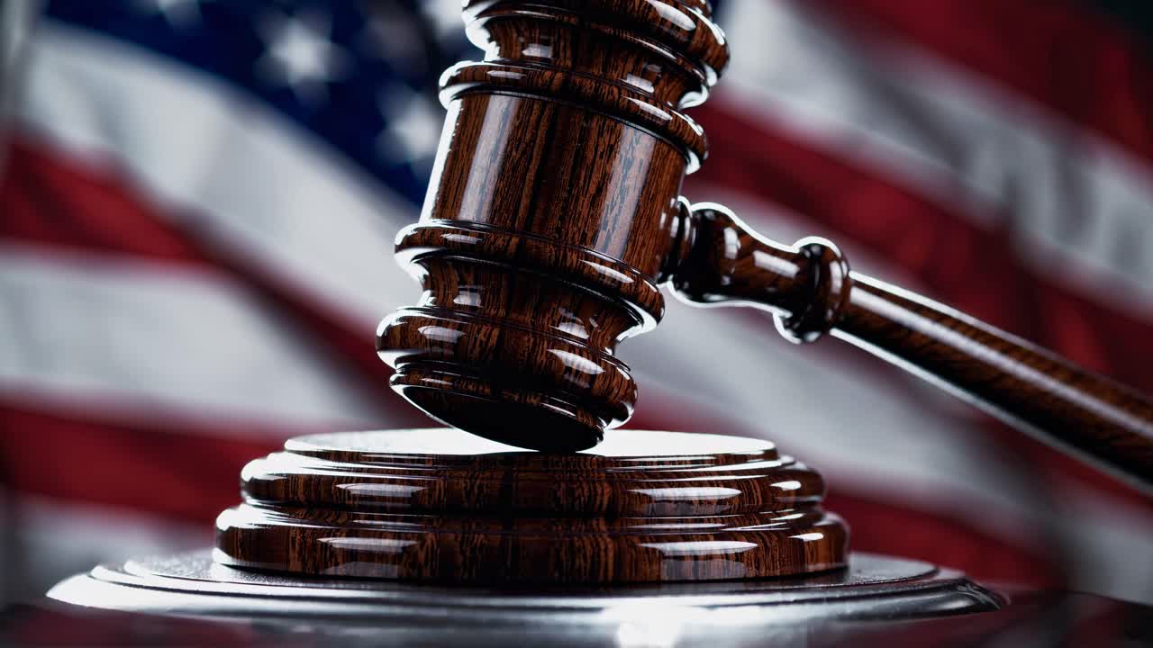 Wooden gavel on a sound block with a blurred American flag in the background, symbolizing justice