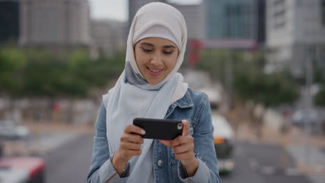 Retrato-Joven-Mujer-Musulmana-Feliz-Usando-Un-Teléfono-Inteligente-Tomando-Fotos-En-La-Ciudad-Disfrutando-Compartiendo-Experiencias-De-Viajes-De-Vacaciones-Usando-Hijab-Velo-Estilo-De-Vida-Moderno-Fondo-Urbano