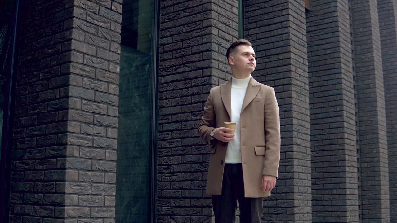 카메라를 바라보는 사무실 근처의 커피와 함께 갈색 코트를 입은 잘생긴 사업가