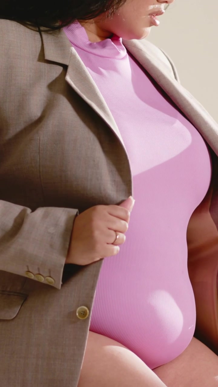Vertical video: Camera moving woman fixing tan blazer and closing, posing and revealing bodysuit