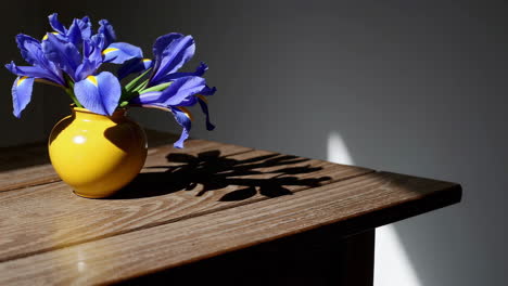 blue irises in a yellow vase on a wooden table with shadows