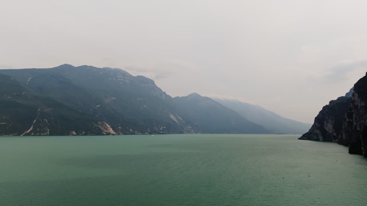 Stunning drone footage of Lake Garda with crystal-clear waters in the foreground and towering mountains in the background, capturing the natural beauty of northern Italy