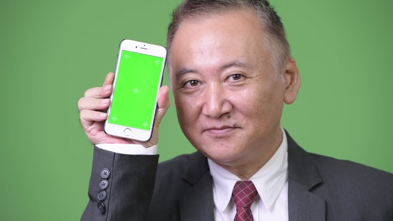 성숙 한 일본인 사업가 가 카메라 에 전화 를 보여주고 있다