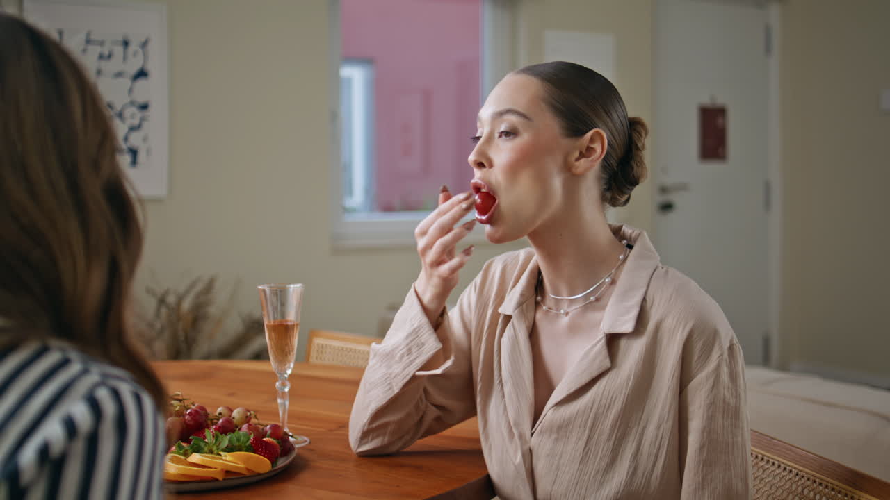 Woman eating grape home meeting with friend closeup. Smiling ladies talking