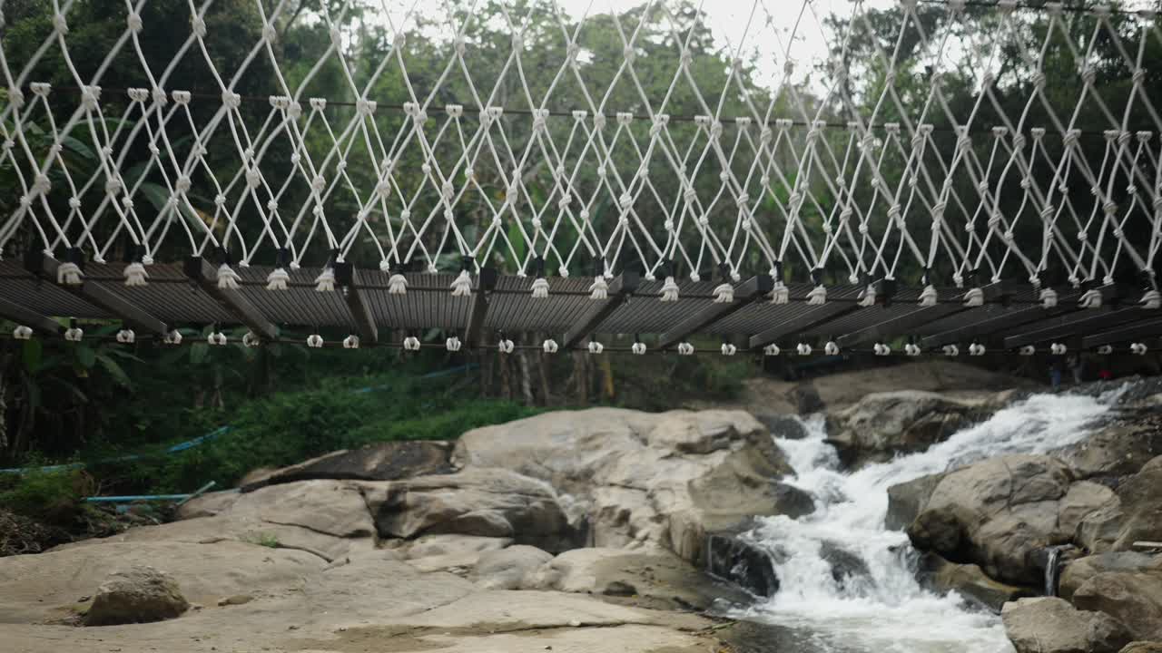 Suspension Bridge Over a Rocky River and Waterfall in a Lush Forest
