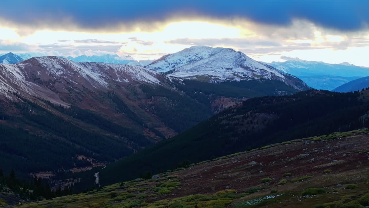 Vista drone di una vasta valle montana, con pianure rocciose e cime innevate in lontananza.