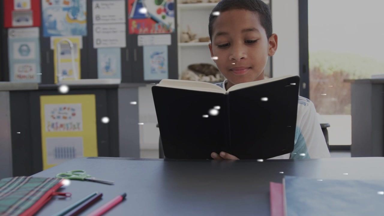 Student boy opening black book, reading in classroom, white particles floating across boy for study