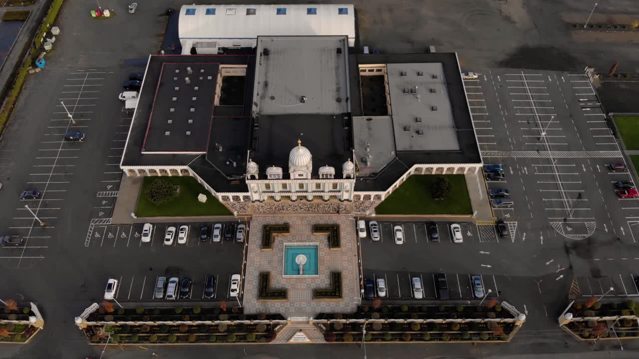 Drone 4K of front facade of Sikh temple with beautiful and elaborate sculpture and symmetrical architecture revealing the blueberry farmland and parking lots around the building