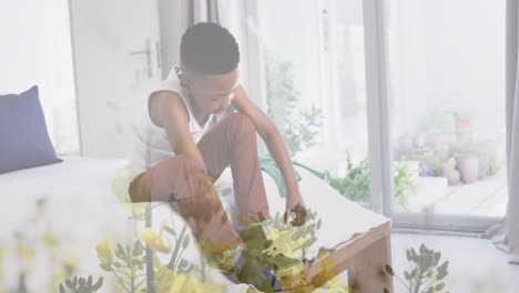 animation of plants over african american boy tying shoe on bed