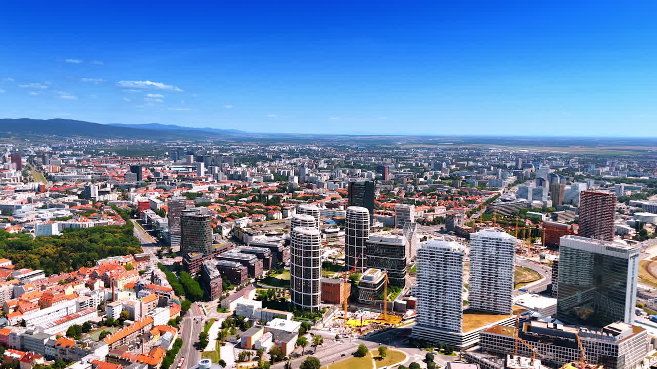 Bratislava, Slovakia, 2 June 2025: Bratislava skyline in blue skies. Aerial view of sunny Bratislava, highlighting modern buildings and greenery with distant mountains