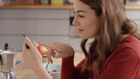 mujer hermosa navegando por internet en pantalla táctil teléfono inteligente en casa en la cocina