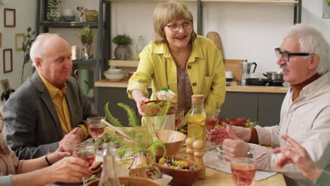 senior woman giving dish to guests at holiday dinner