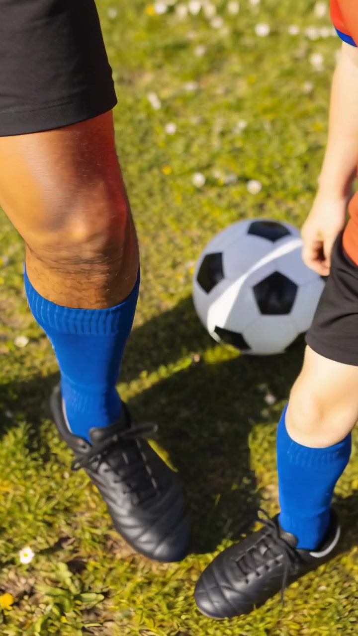 Video verticale: Allenatore e bambino che allacciano le scarpe da calcio preparandosi a giocare sull'erba, bambino con maglietta rossa vicino al pallone
