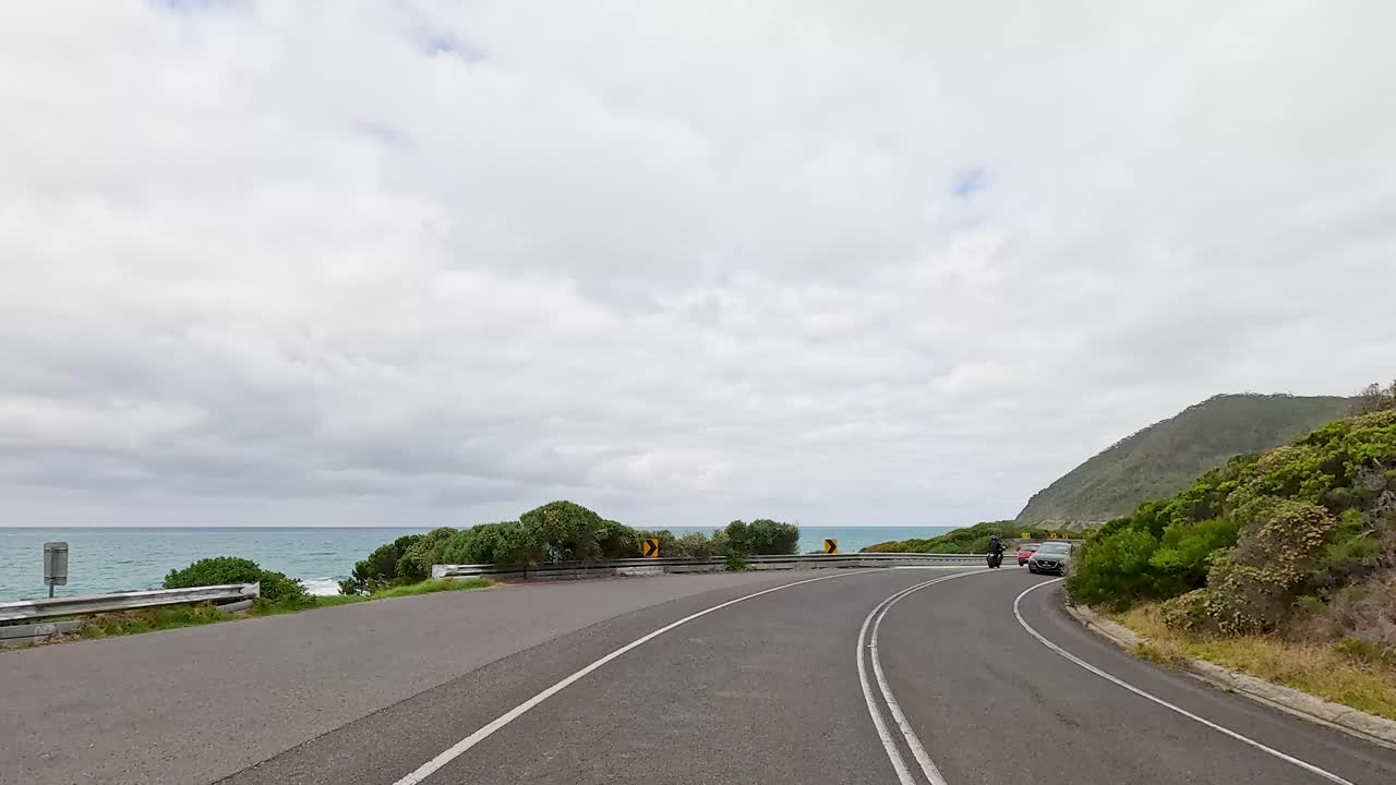 A 14-second drive along Great Ocean Road, showcasing coastal views, lush greenery, and winding roads under overcast skies