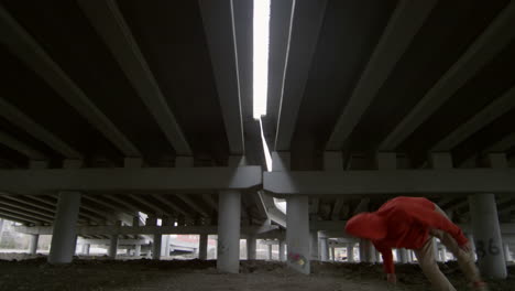 parkourist performing trick under urban bridge