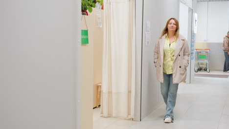 confident woman in casual denim over striped tee walks down clean laundromat corridor, hands in pockets, smile, purposeful stride, bright indoor setting with curtain, signage, carts, modern ambiance
