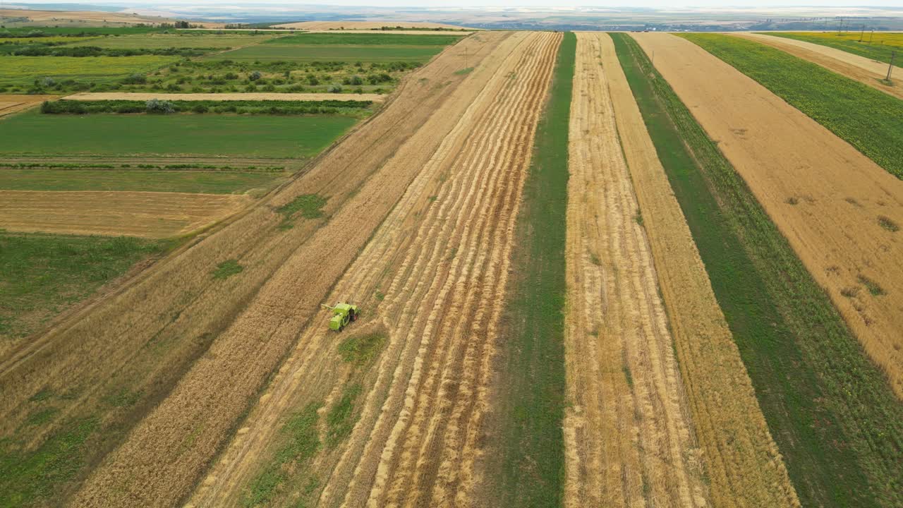 Wide aerial drone panning shot of two harvest combines moving over grain fields