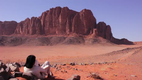 an arab man in traditional clothing sits and contemplates the desert of wadi rum jordan