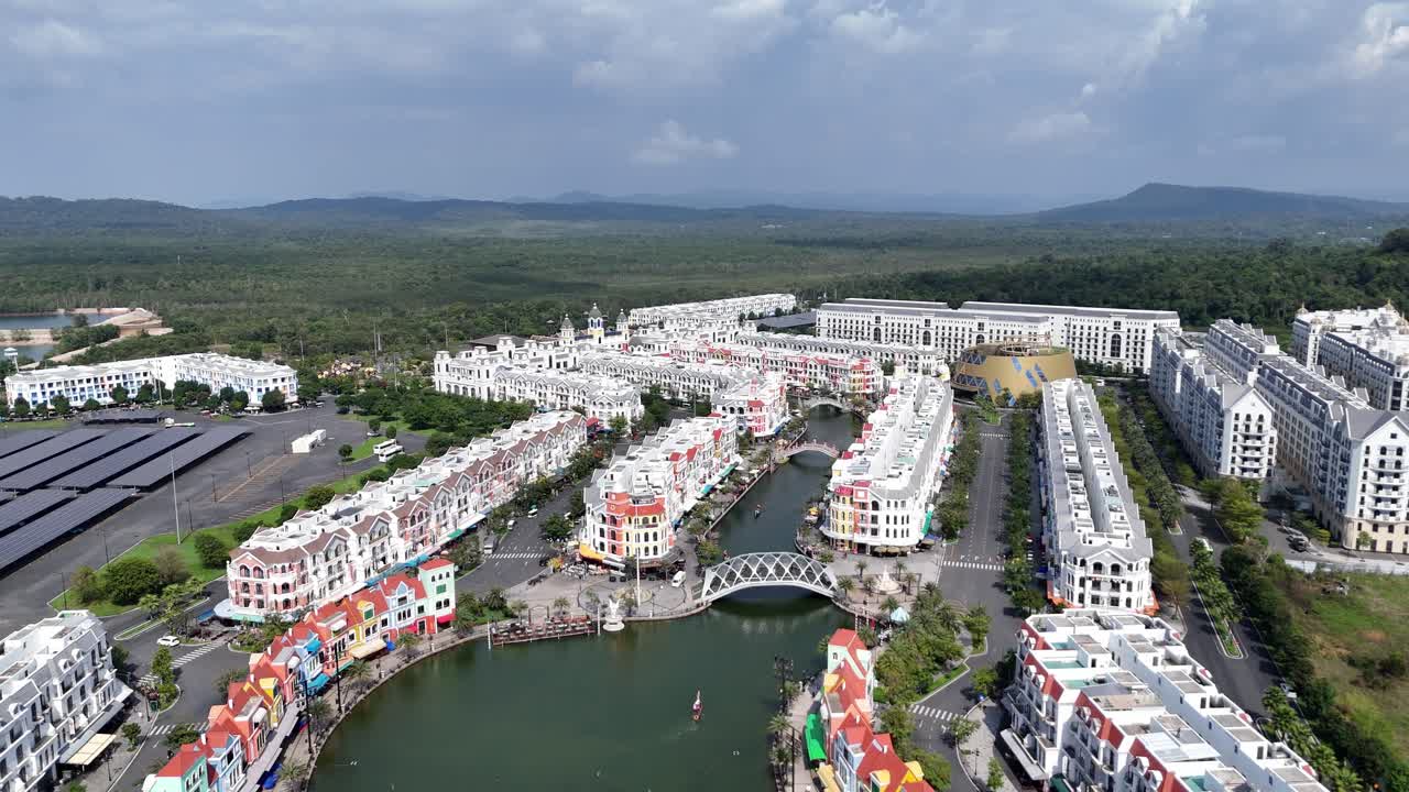 Aerial video shows architectural style, where rows of colorful buildings stand closely along both banks of a waterway. A charming bridge connecting the vibrant districts. Newly built town.