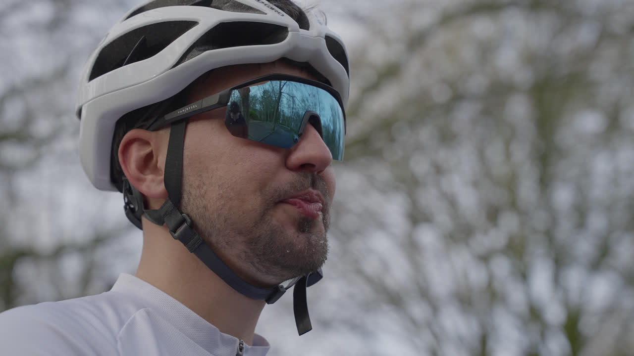 Man wearing helmet and sunglasses drinking from sports bottle while cycling