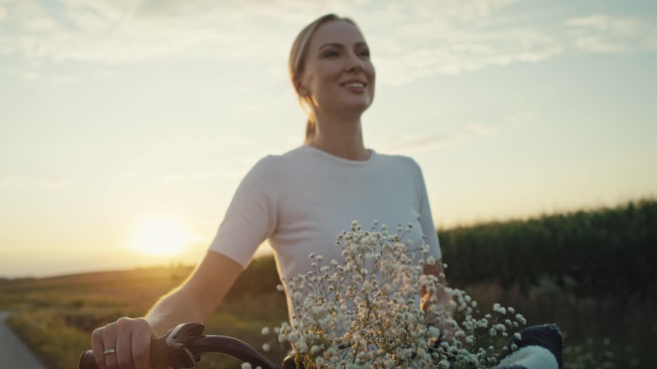 una allegra donna caucasica di mezza età che cammina con una bicicletta al tramonto sulla strada del villaggio.