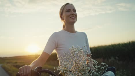 Cheerful-caucasian-woman-of-middle-age-walking-with-a-bike-on-sunset-on-village-road.