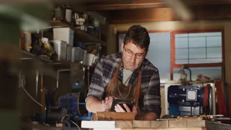 Focused-caucasian-male-knife-maker-in-workshop-using-tablet