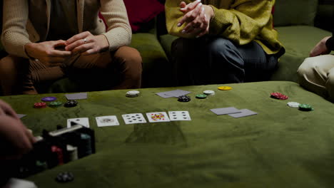 la cámara se enfoca en las manos de un grupo de amigos que toman cartas y fichas de póquer en la mesa