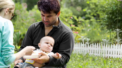 Eltern-Füttern-Ihr-Baby,-Das-Auf-Dem-Gras-Sitzt