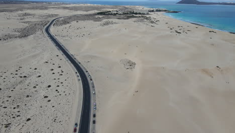 A-winding-road-through-corralejo-sand-dunes-with-the-ocean-beside,-fuerteventura,-aerial-view