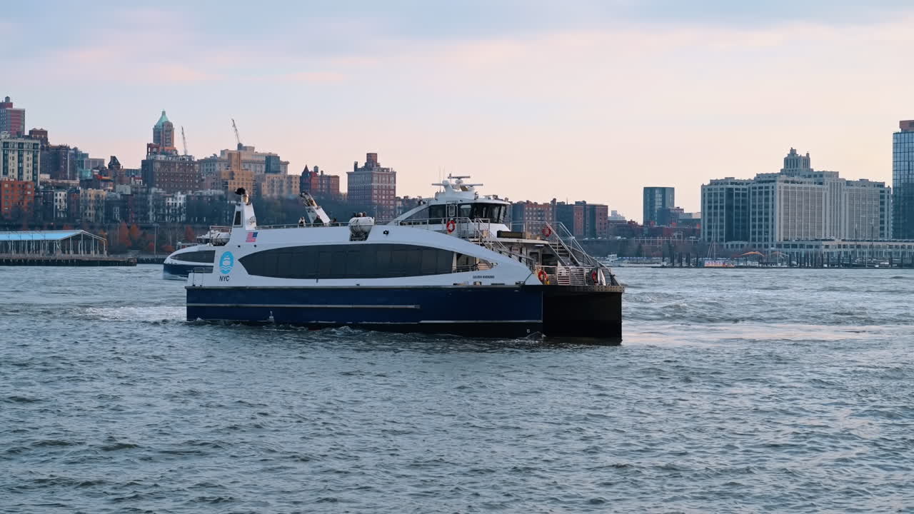 New York, USA, 5 dicembre 2025: traghetto blu e bianco sull'acqua con sfondo di paesaggio urbano. Un traghetto blu e bianco di NYC Ferry si muove sulle acque agitate del fiume, con il paesaggio urbano residenziale di Brooklyn sullo sfondo.