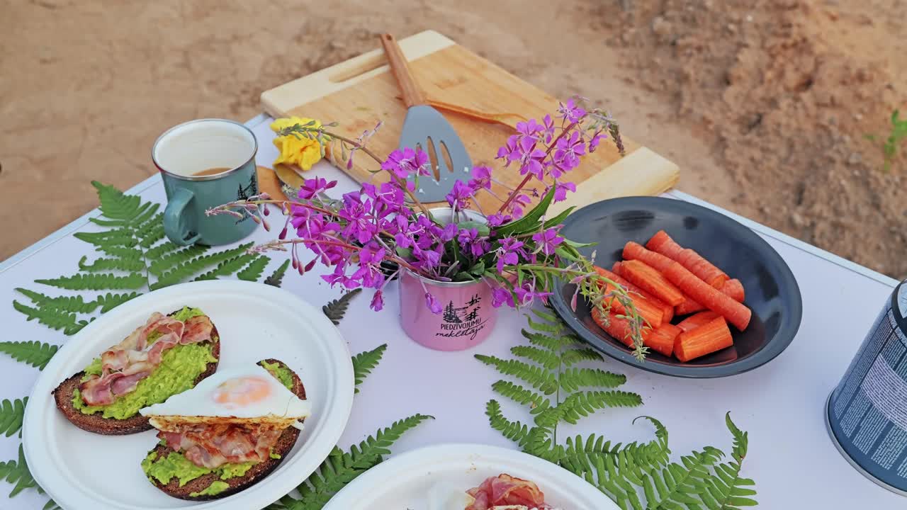 Colorful camping breakfast table outdoors, eggs bacon avocado toast and carrots